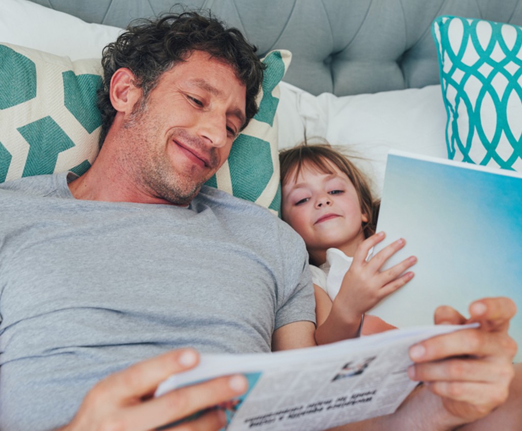 a happy father and daughter resting in a bed while reading books