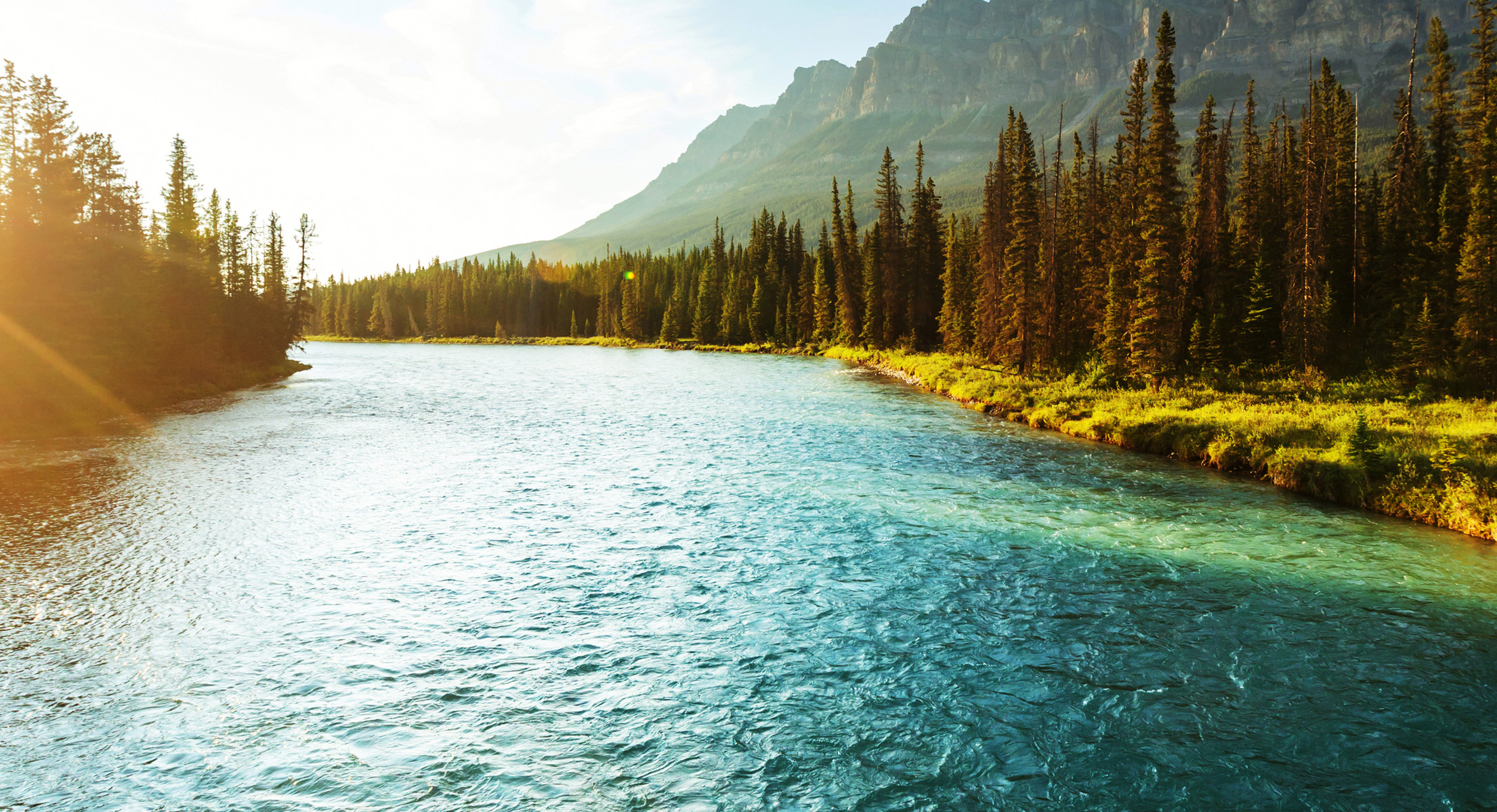 a landscape of fresh water along a tree covered bank and rolling mountains